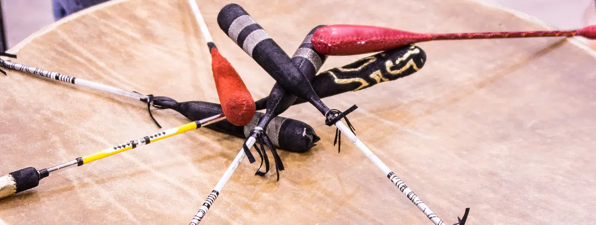 A collection of Indigenous drumsticks resting on a large drum.